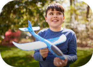 Smiling child holding a blue foam toy airplane outdoors on a sunny day.